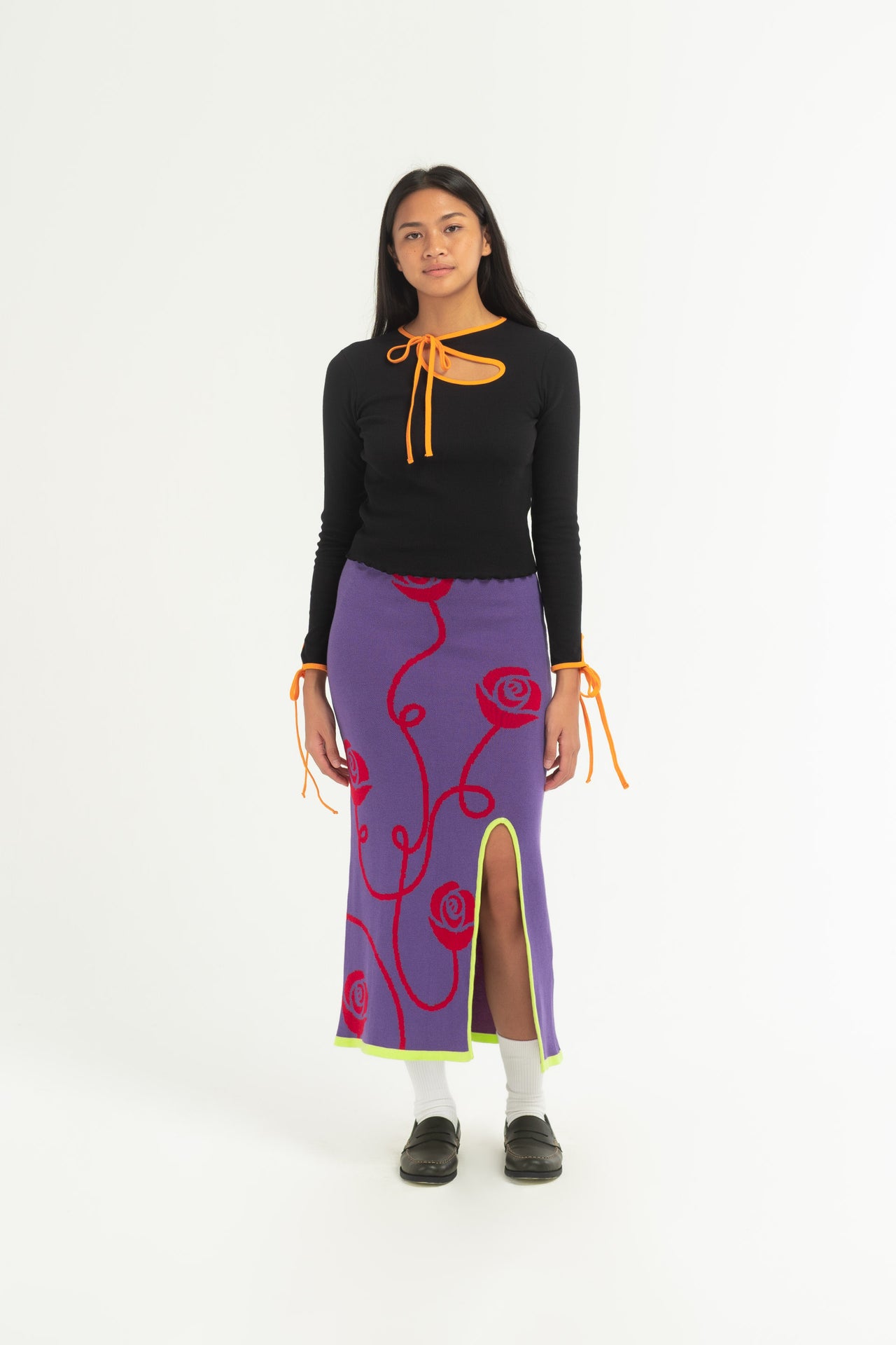 The Sweet Rose Split Skirt is a  purple knitted long skirt that features a red rose print, split at the front and bright green trim. 