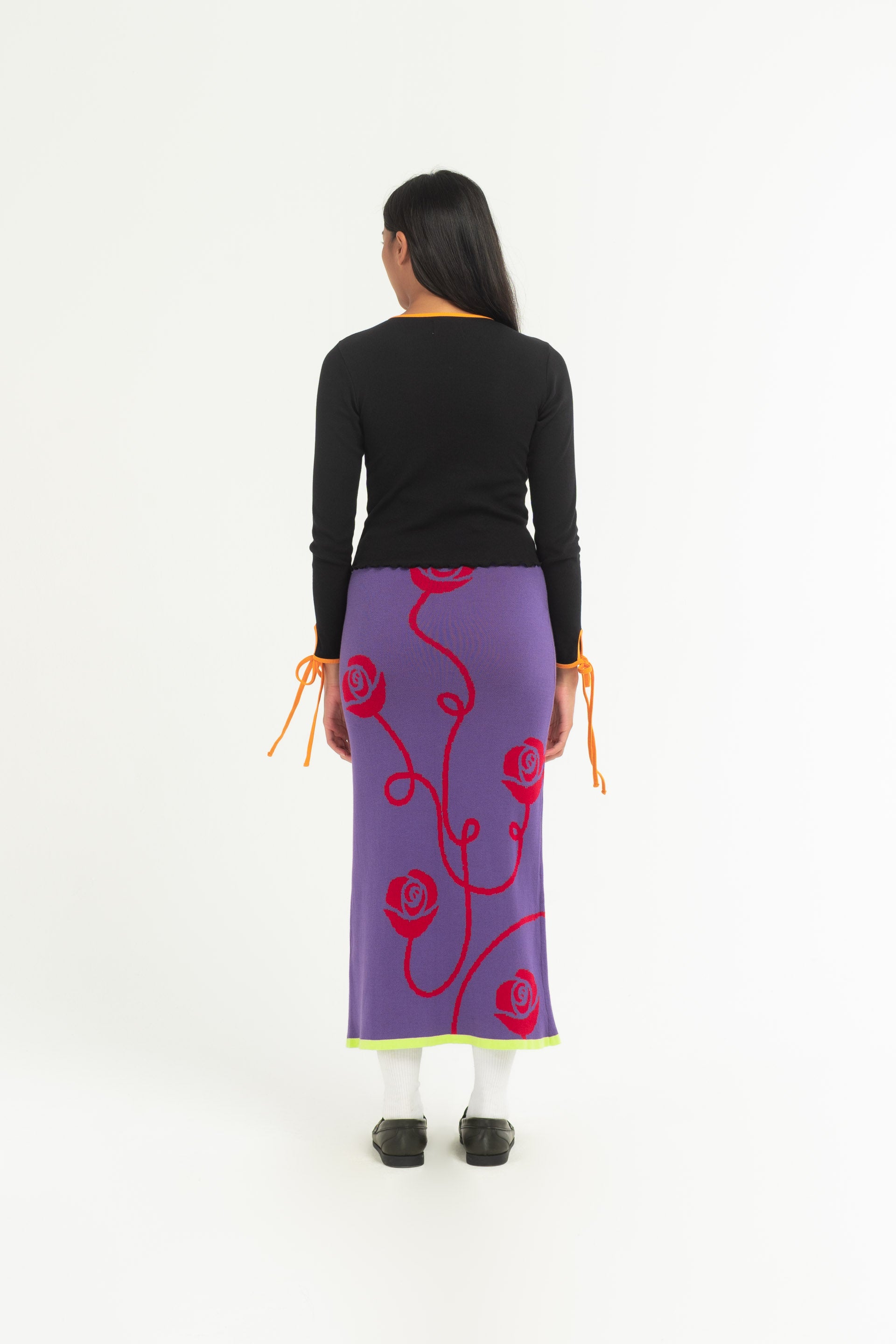 The Sweet Rose Split Skirt is a  purple knitted long skirt that features a red rose print, split at the front and bright green trim. 